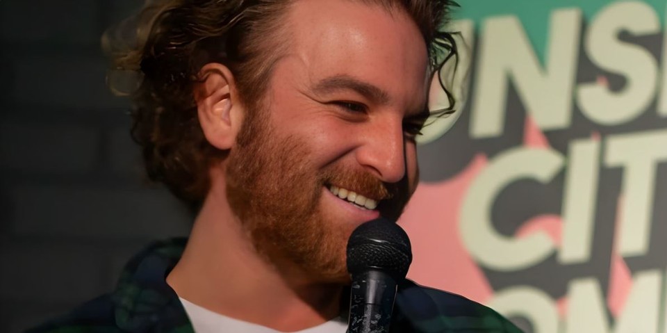 Jake Polin smiling into a microphone on stage at Sunshine City Comedy Club